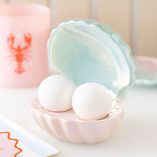 A pastel shell-shaped salt and pepper shaker holder with an iridescent finish, holding two white pearl-style ceramic shakers.