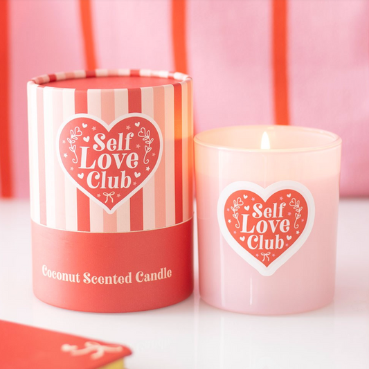 A pink coconut scented candle with a Self Love Club heart design beside a matching striped gift box in pink and red tones.