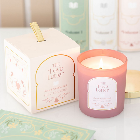 A pink rose and vanilla musk scented candle in a blush glass jar beside a matching decorative gift box with gold detailing and The Love Letter label.