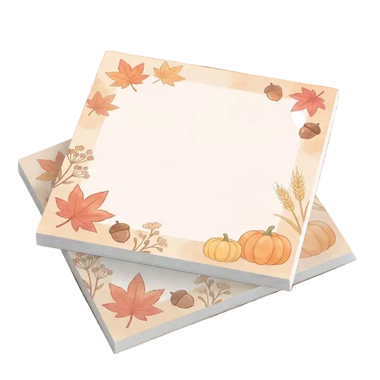 Three square sticky note pads with an autumn-themed border featuring maple leaves, pumpkins, acorns, and wheat, arranged on a wooden tabletop.