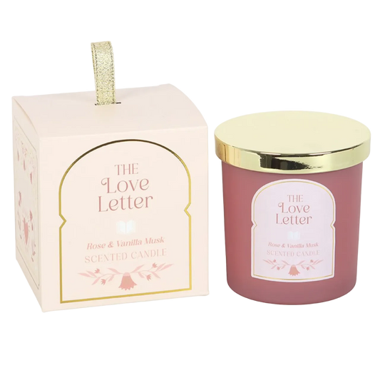 A pink rose and vanilla musk scented candle in a blush glass jar beside a matching decorative gift box with gold detailing and The Love Letter label.