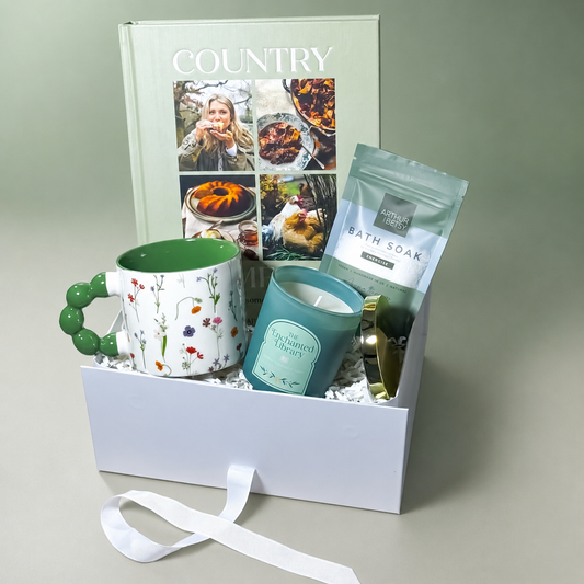 Gift box with a mug, candle, and bath soak on a light gray background