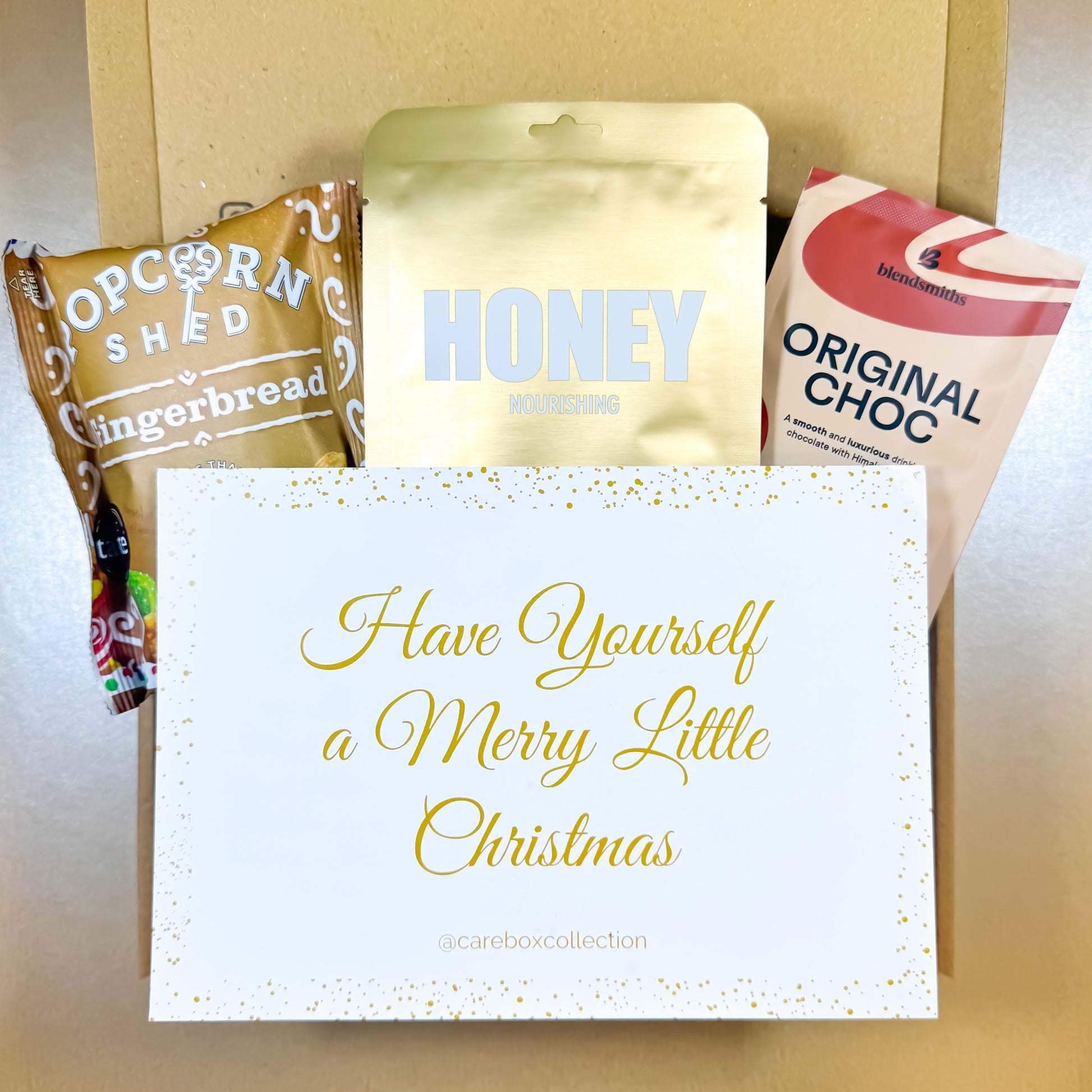 Holiday Hug Christmas Care Box with gingerbread popcorn, honey face mask, hot chocolate and a festive handwritten Christmas notecard.